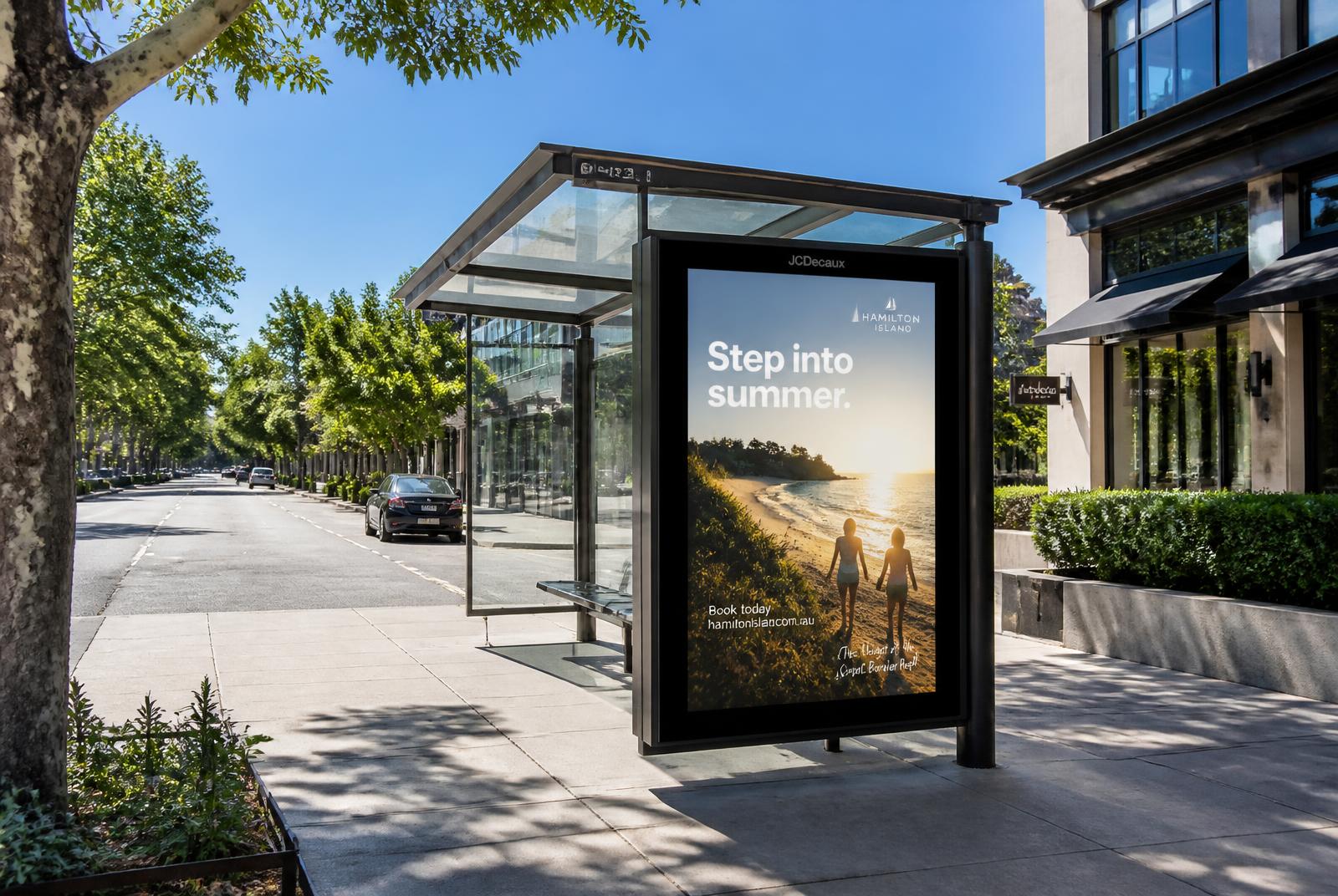 Glass bus shelter with a digital advertising panel on a sunny city street